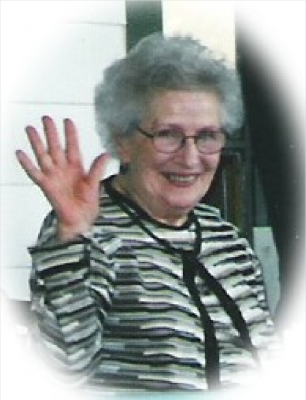 A woman wearing a striped cardigan is smiling and waving at the camera.