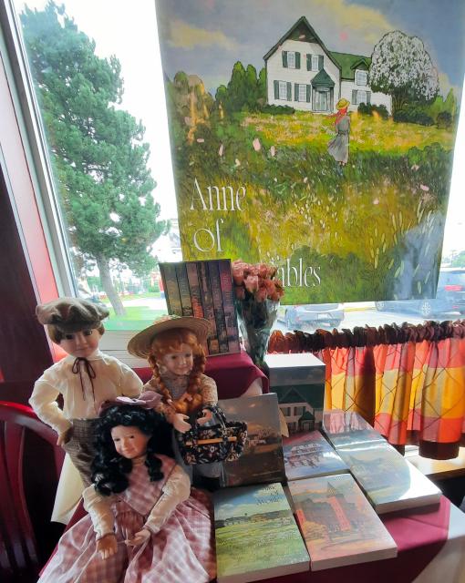 Table display of three dolls and Thai book covers with poster of Anne of Green Gables behind.
