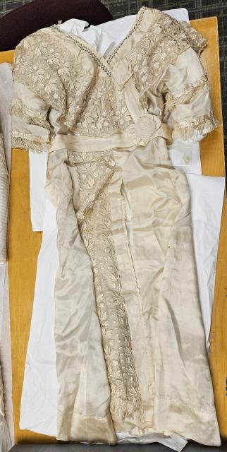 Ivory silk and lace wedding gown detailed with tasselled short sleeves, fabric rosettes, pleated waistband, and steel-cut beading at the neckline.